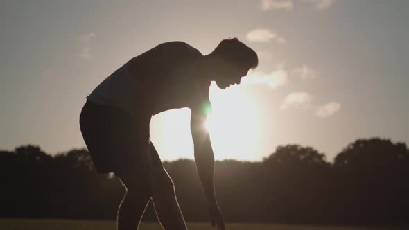 Man Stretching His Legs Before a Run Whilst Being Silhouetted By The Evening Sun In Slow Motion