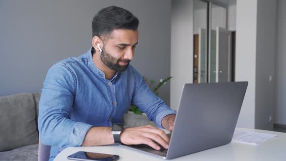 Young Adult Smiling Indian Businessman Working on Laptop Computer at Home Office