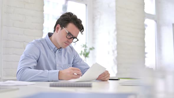 Attractive Working Young Man Reading Documents in Office