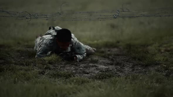 Soldier crawling under low barbed wire at an obstacle course, its muddy