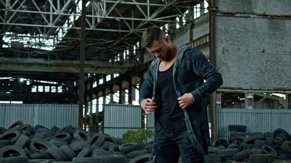 Bearded man in military clothing stands in abandoned place. 