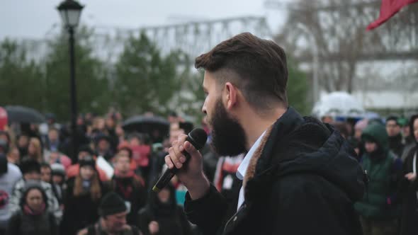 Male Spokesperson on Stage with Mic Gives Address to Crowd with Russian Banners