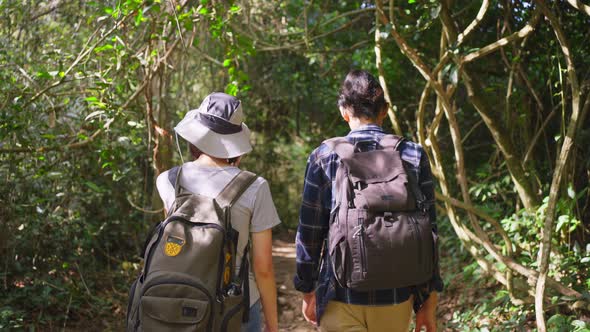 Follow back view, young Asian man and Caucasian woman friend traveling in the forest together.