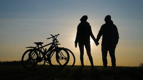 Couple Tourists Ride on Bike on the Road. Two Silhouettes of Cyclists on a Sunset Background. Sport