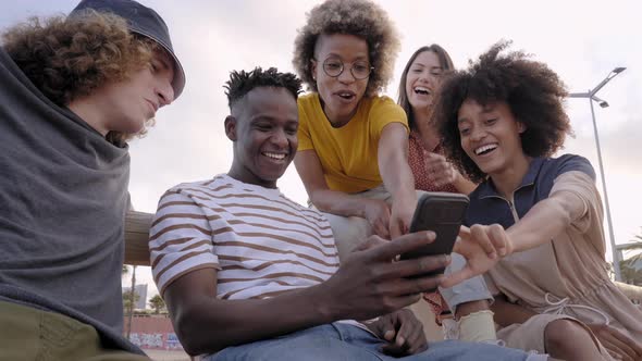 Happy Smiling Teenage Friends Laughing Outside at Something in Smartphone or Mobile Phone