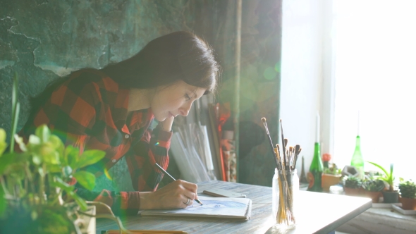 Young Woman Artist Painting Scetch on Paper Notebook with Pencil. Bright Sun Flare From Window