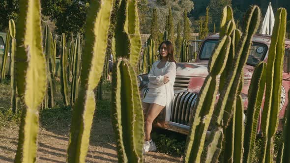 Young Asian Woman Stands By an Old Pickup Truck at Sunset and Looks at the Camera