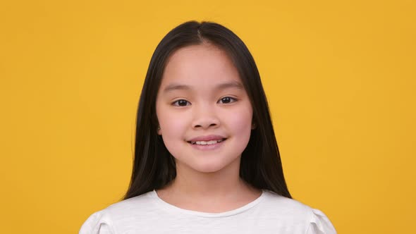 Close Up Studio Portrait of Adorable Pretty Preteen Asian Girl Smiling to Camera Posing Over Orange