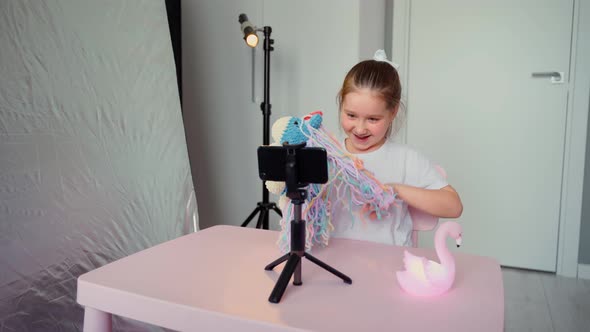 Young little girl blogger writes a video about knitted toys on her blog in a home studio