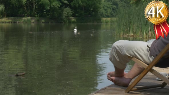 an Adult Man Sits on a Chair Near a Lake