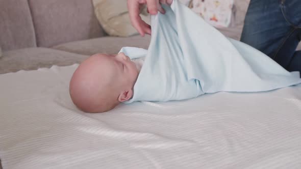 Father Swaddles a Newborn Son in a Blue Diaper