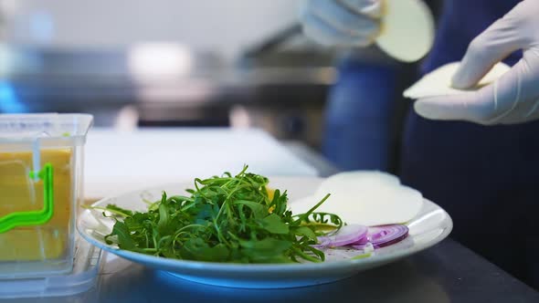 Arugula, cheese and onion on plate. Ingredients for tasty salad. Closeup.