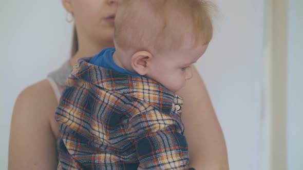 Mommy Holds Lovely Baby in Arms Against Wall Closeup