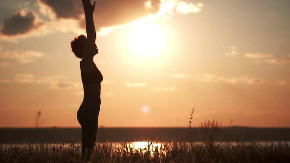 Silhouette of Young Beautiful Girl Practicing Yoga at Sunset