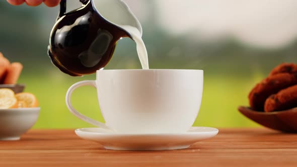 Pouring Milk Into Hot Coffee in White Cup on a Wooden Table