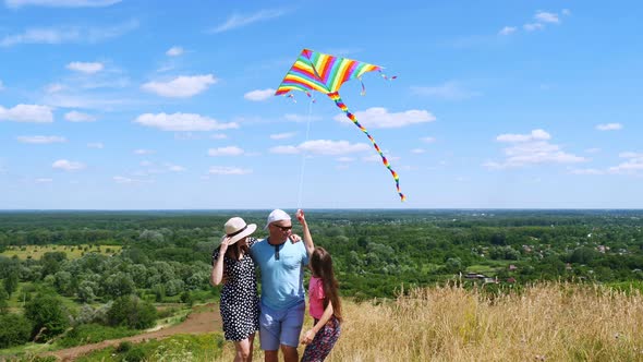 Happy Young Family of Three Fly a Multi-colored Kite, Having Fun, Against Background of Beautiful