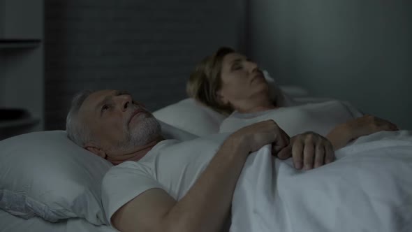 Aged Man Lying in Bed Awake, Looking at Woman Sleeping Beside Him, Annoyance