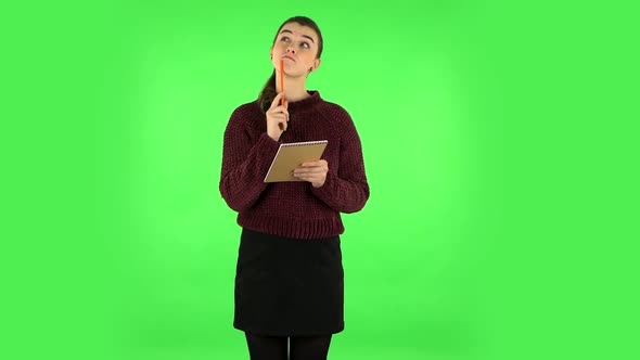 Girl Stands and Thinks, Then Writes with Pencil in Notebook. Green Screen