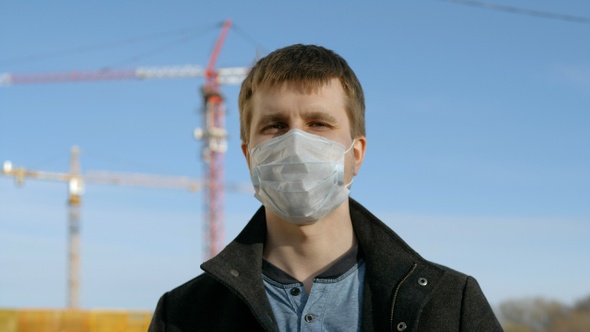 Adult man wearing medical mask standing next to construction site.