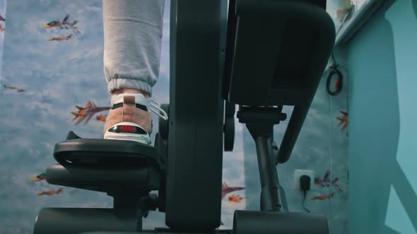 Young Girl in Sneakers is Engaged in an Orbitrek at Home Bottom View