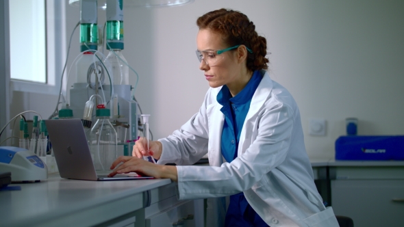 Female Scientist Working in Laboratory. Lab Worker Typing Report on Computer alt