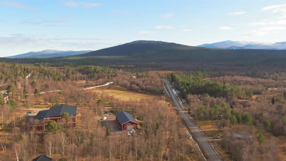 Red Farm Buildings In Swedish Alpine Spruce Conifer Forest Near Snowcapped Mountains.