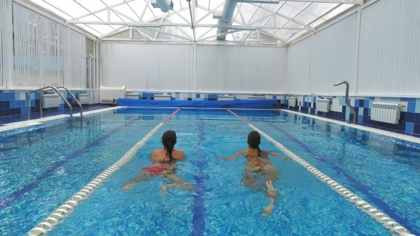 Two Young Women Talking and Swimming in the Pool