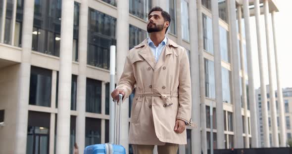 Low Angle View of Handsome Businessman with Suitcase Looking Away While Waiting Taxi Outdoors