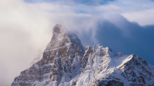 Clouds Flowing Over Snowy Mountain Peak at Sunrise