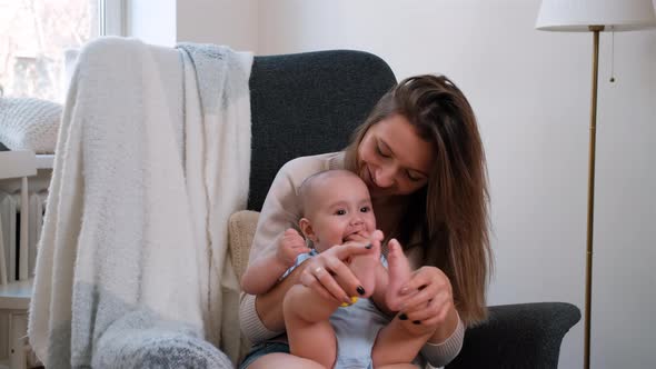 Young Mother Sits in Armchair with Her Cute Baby