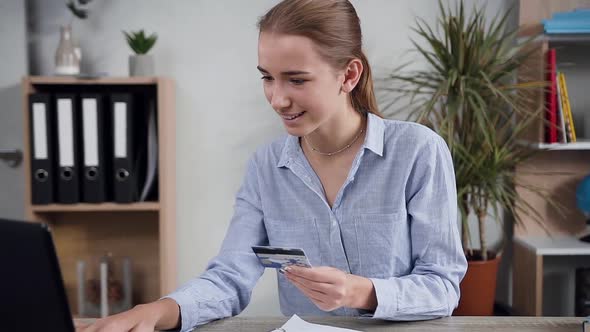 Woman Sitting at the Table and Making Online purchases using laptop and her credit card