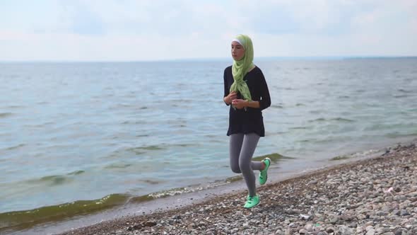 A Young Muslim Woman in a Burqa and Sports Sneakers Is Running Around the Sea