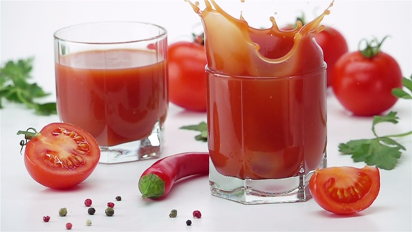 Ripe Tomato Falls into a Glass of Tomato Juice