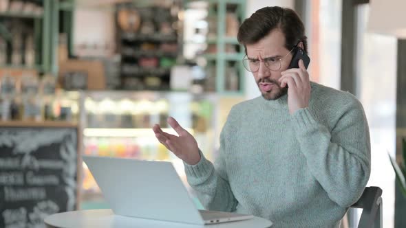 Angry Young Man with Laptop Talking on Smartphone