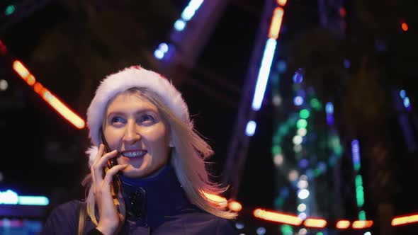 a woman chatting on her smartphone wearing a Santa hat is a night city.