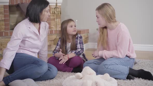 Portrait of Happy Caucasian Family Sitting on Soft Carpet in Front of Fireplace and Talking. Mother