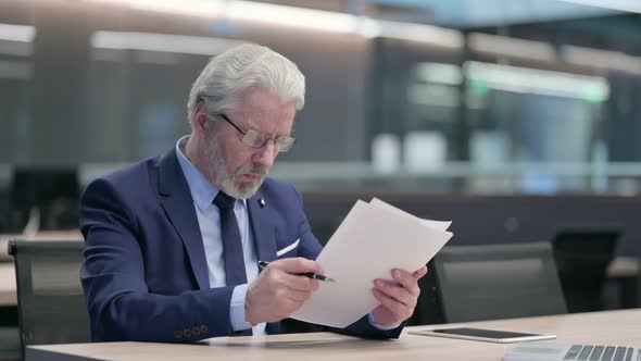 Old Businessman Reading Documents in Office