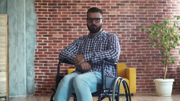 Thoughtful Bearded Disabled Man with Glasses is Sitting in Wheelchair Sad and Depressed