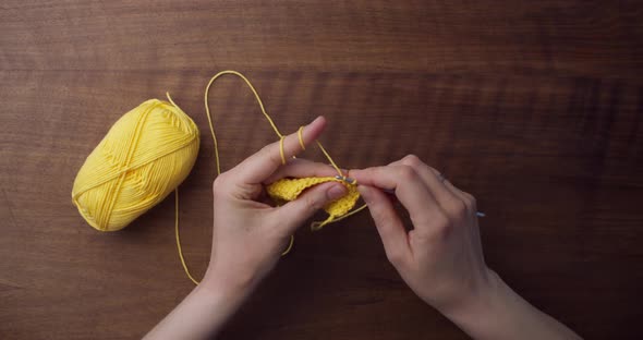 Time-lapse of the crocheting process. Caucasian hands grabbing a yellow piece of wool and starting t