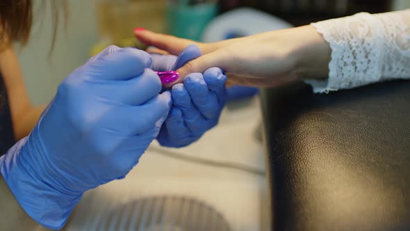 Unrecognizable Person in Gloves Paints Nails of Young Woman in Salon