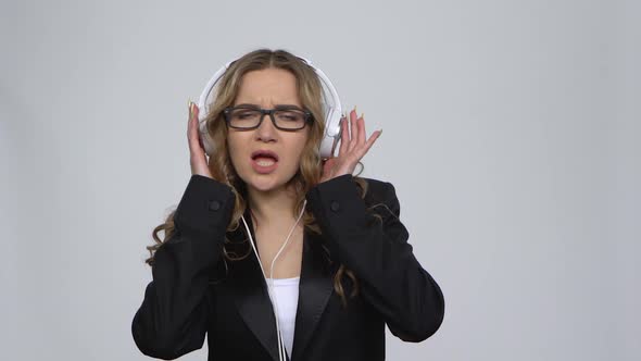 Woman Dancing Enjoy Music in Big White Earphones on Gray Background at Studio