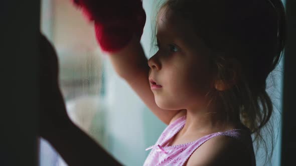 Girl Wipes Window with Rag Helping Mother to Clean House