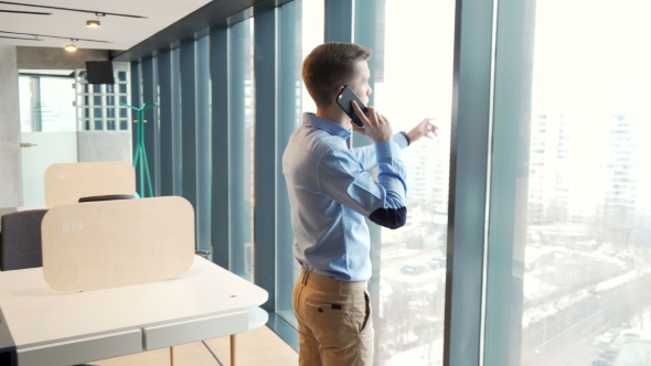 Young Businessman Talking on Cellphone Standing By Window at Coworking Office