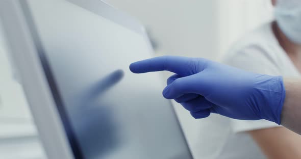 A Doctor in Hygienic Gloves Uses a Tablet Moving His Finger Across the Screen