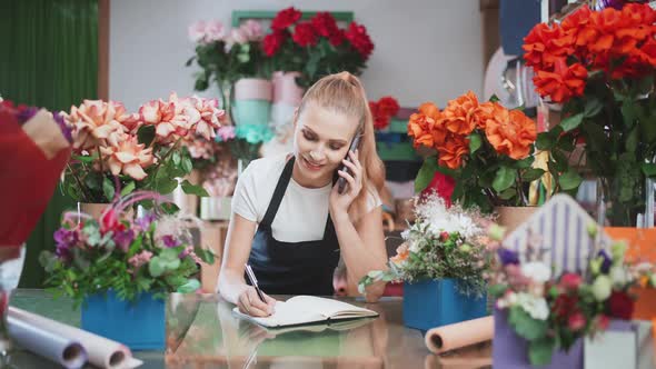 Florist Female Discusses the Order By Talking on the Mobile Phone and Using a Notepad in a Flower