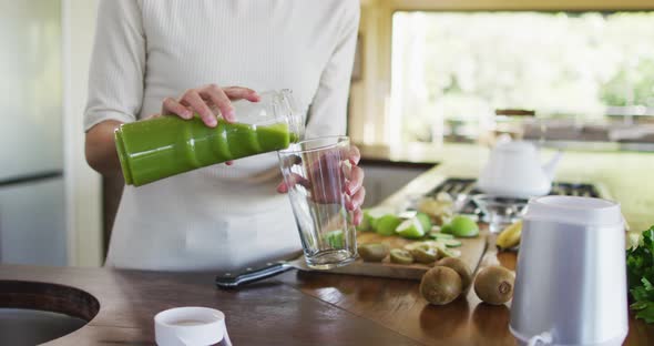 Midsection of biracial woman pouring smoothie to glass in kitchen