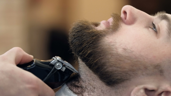 Horizontal Portrait of a Barber Shaping Beard of His Client Using a Trimmer