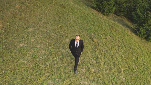Businessman Walking at Green Grass Mountain Hill Top Down Aerial
