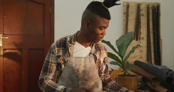 African american craftsman in checked shirt and apron smiling in leather workshop