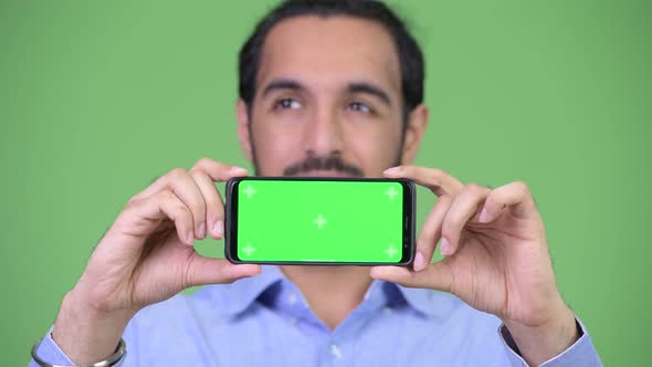 Young Happy Bearded Indian Businessman Thinking While Showing Phone